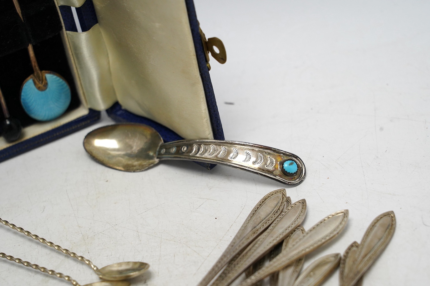 A set of ten George V silver coffee spoons, Birmingham, 1931, a later cased set of six silver and polychrome enamel bean end coffee spoons, a turquoise set sterling spoon, and a set of six white metal spoons with hardsto